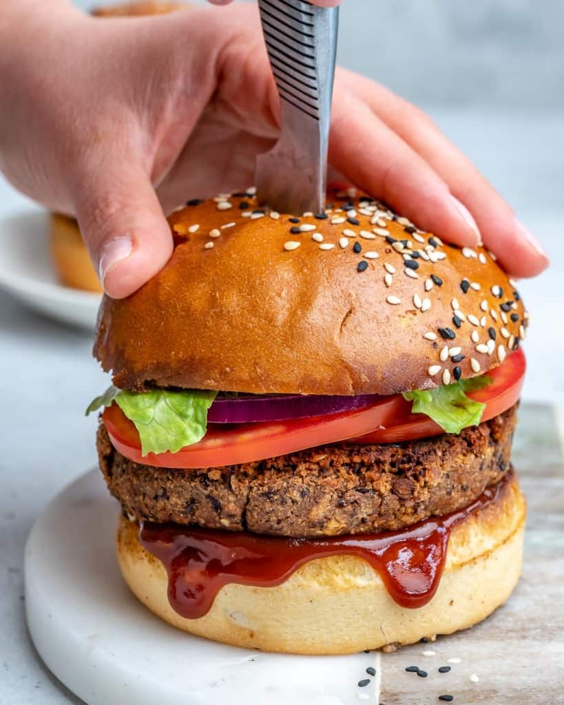 hand holding down a bean burger with knife placed in the middle of the burger 