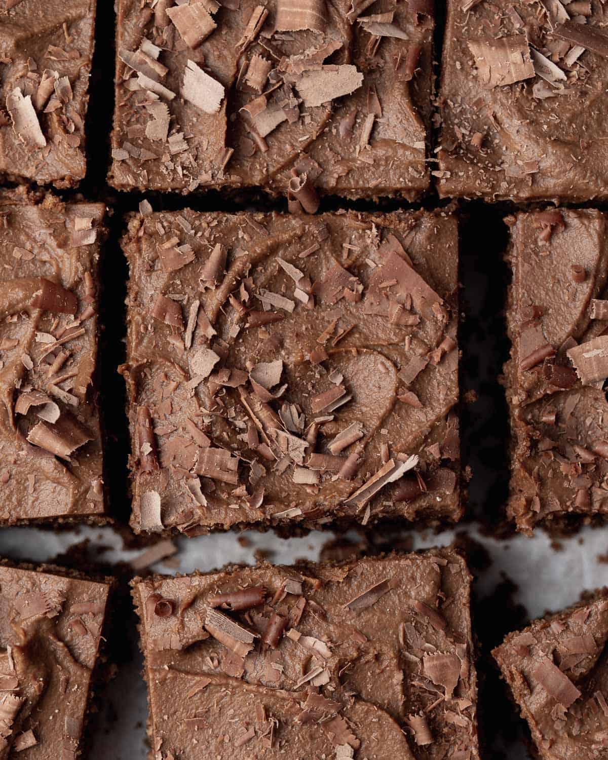 zucchini cake squares topped with frosting and shaved chocolate.