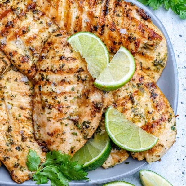 grilled chicken breasts on a plate with lime wedges and cilantro garnish.