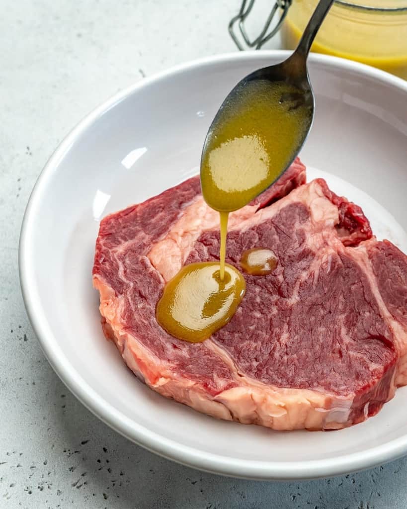 steak marinade being added over a raw steak with a spoon