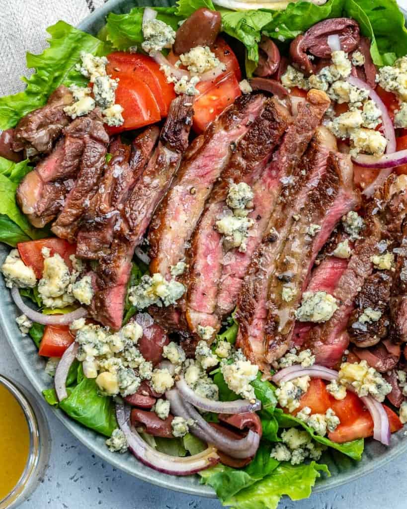 top view of a salad with sliced cooked steak topped with blue cheese