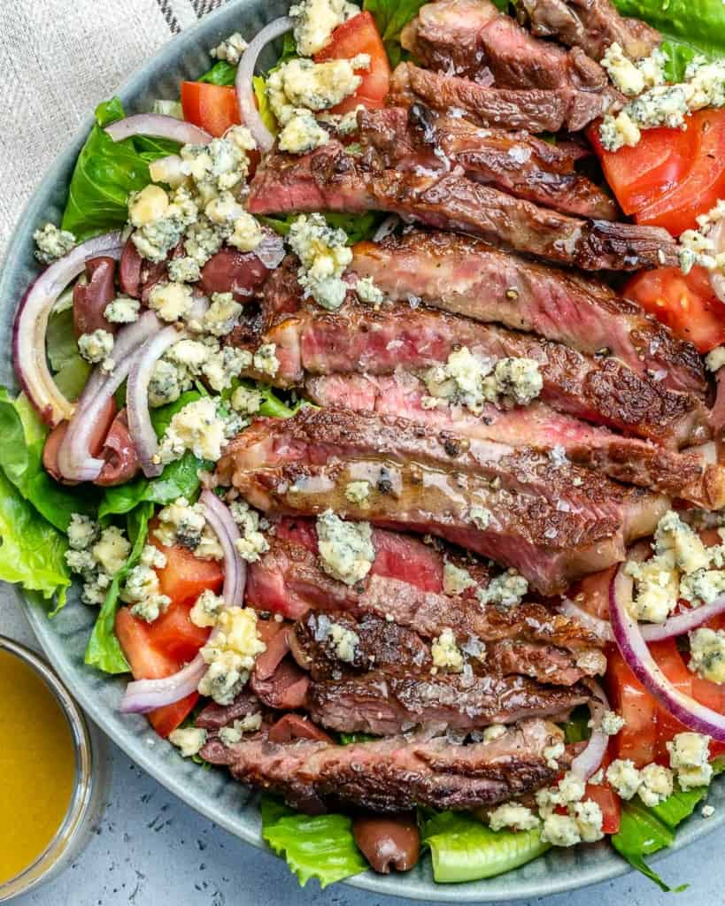 close up view of salad bowl with sliced cooked steak topped with blue cheese 