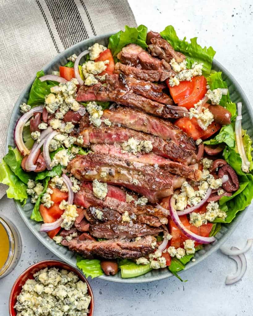 top view of salad bowl with sliced steak, slices red onions, and other veggies, topped with sliced steak