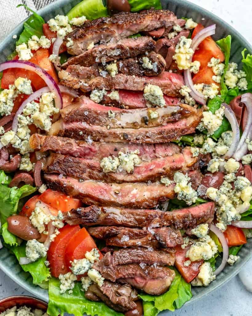 top view of a salad bowl with sliced steak, topped with blue cheese 