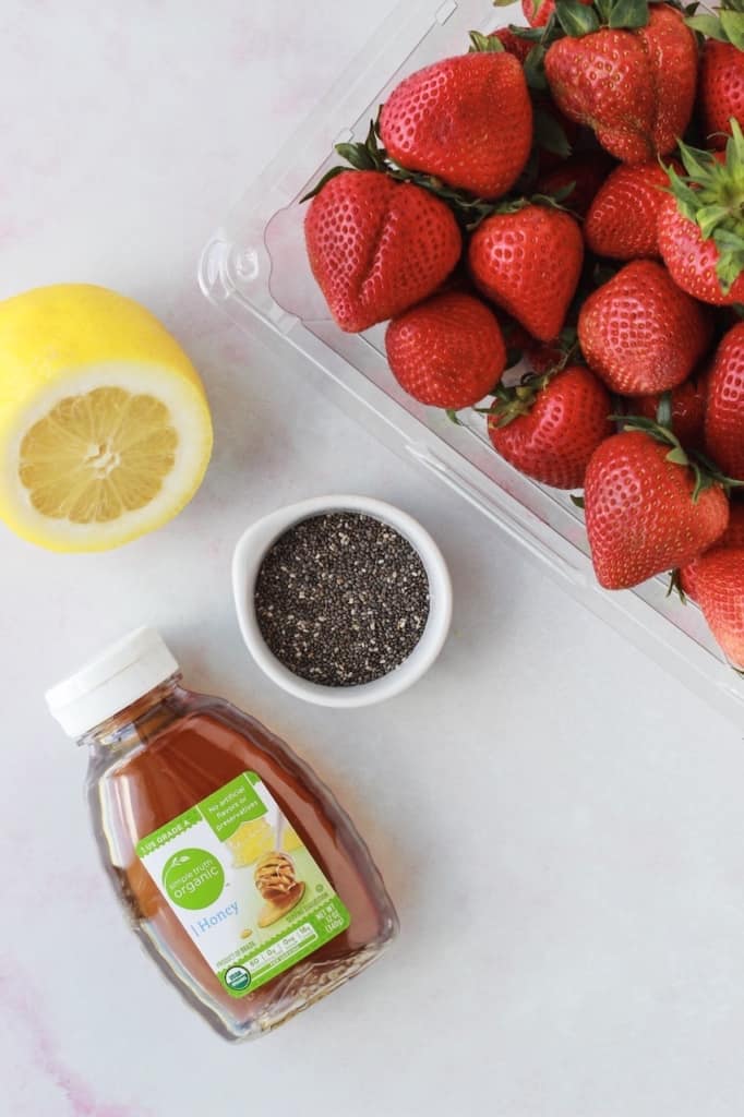 top view of ingredients to make strawberry jam, fresh strawberries, honey, lemon, and chia seeds