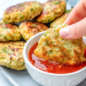 hand dipping a chicken fritter in chili sauce.