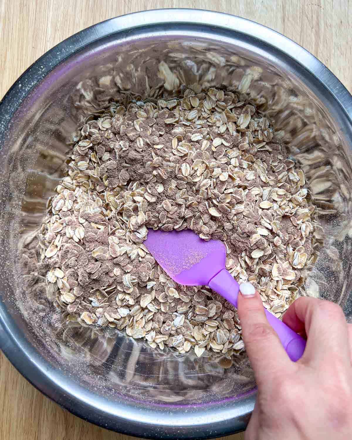 hand holding purple spatula mixing the dry ingredients.