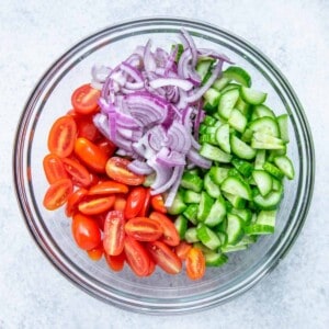 chopped tomatoes, cucumber, and onion in a round clear bowl.