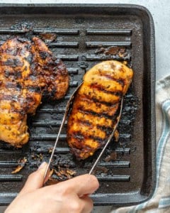 grilled chicken breast over a grill pan with hand holding tongs to grab one