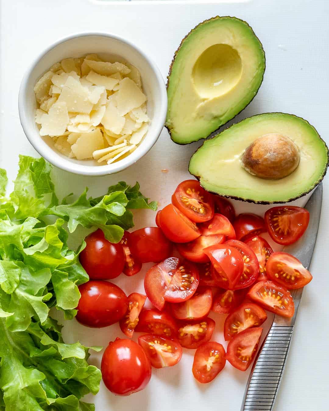chopped lettuce, sliced tomatoes, cheese, and avocado on a cutting board