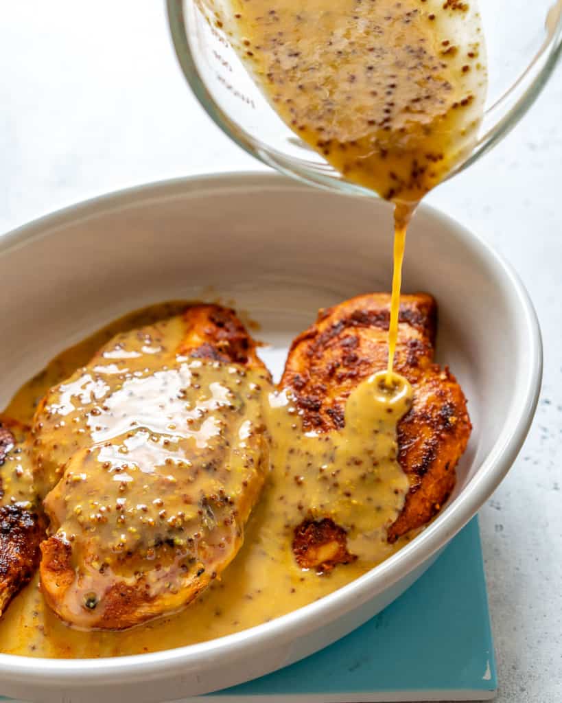 honey mustard sauce marinade added over baked chicken breast in a white baking dish