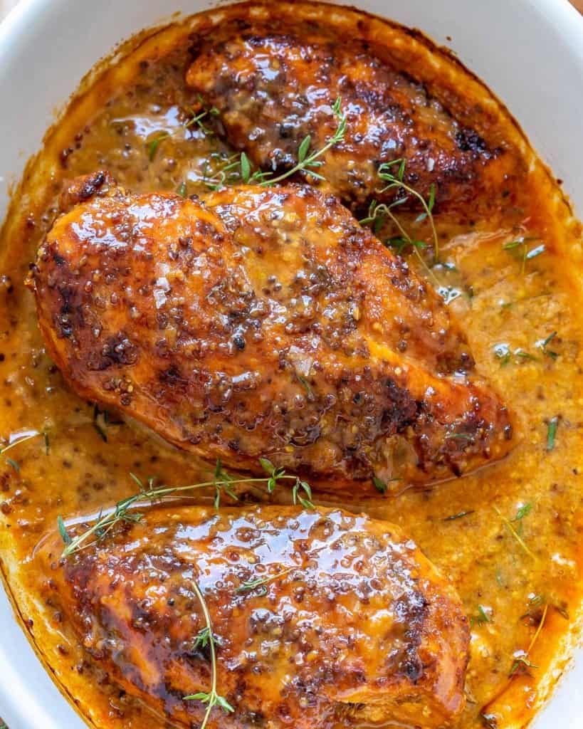 close up view of chicken breast in a honey mustard sauce baked in a white dish
