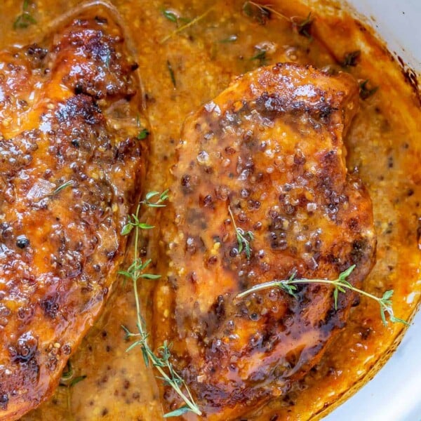 baked honey chicken breast on a white baking dish with thyme garnish