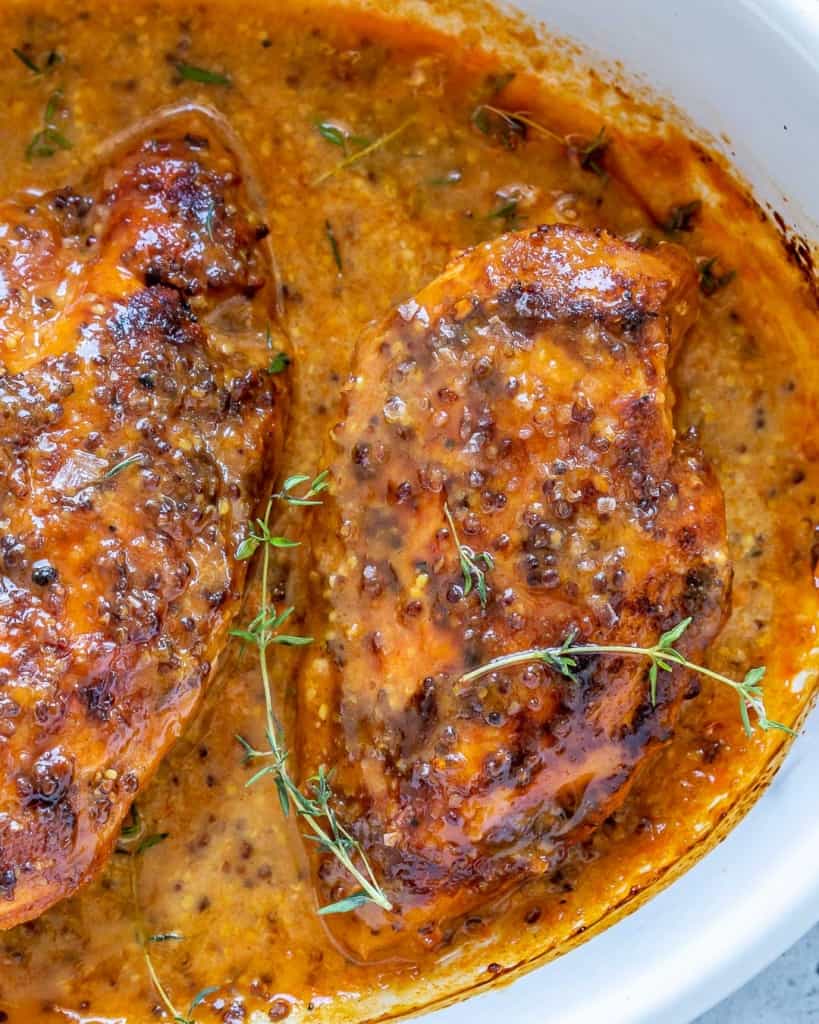 baked honey chicken breast on a white baking dish with thyme garnish 