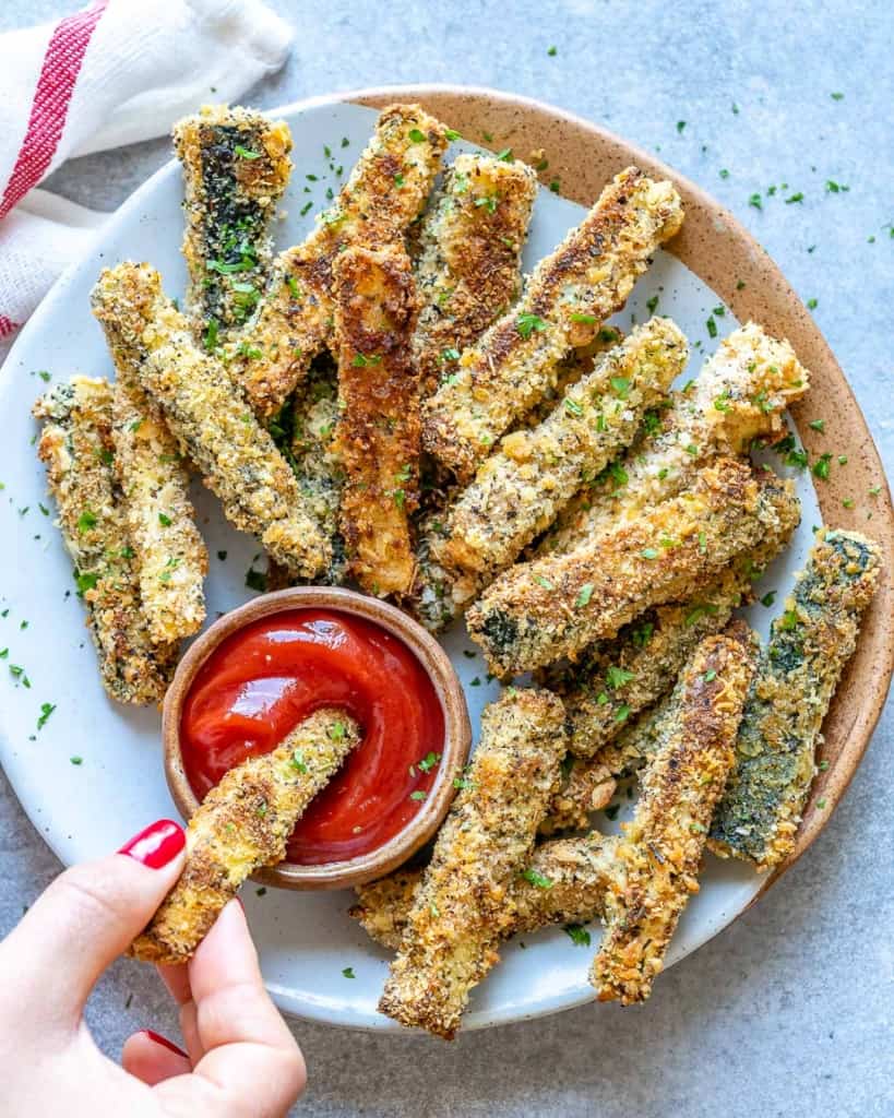 hand holding a zucchini fry in a ketchup dip