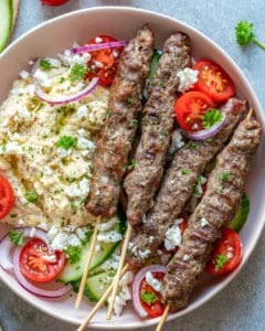 top view of 4 skewers of kafta on a plate with hummus