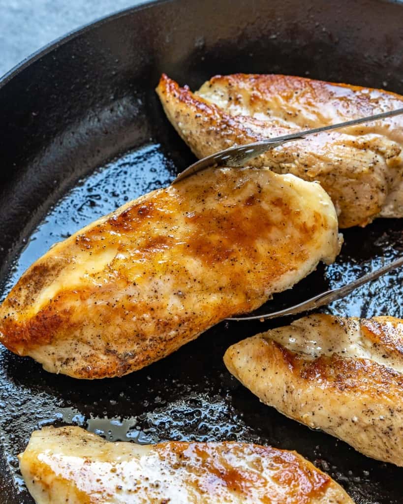 tongs grabbing a cooked chicken breast from skillet 