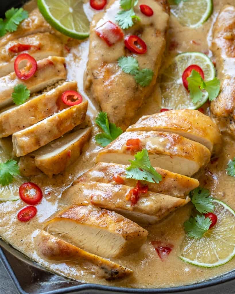 close up sliced creamy coconut chicken breast garnished with chili peppers 