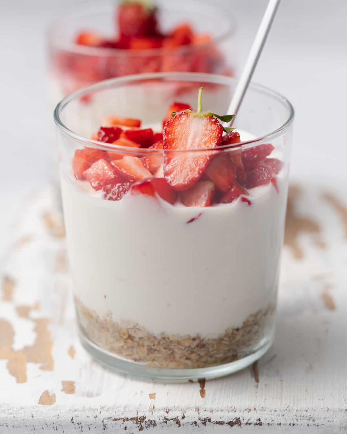 a clear cup with layered no-bake cheesecake, bottom oat layer, cheesecake filling for the middle layer, topped with fresh strawberries.