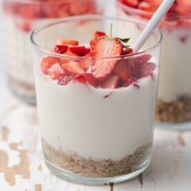 a clear cup with no bake cheesecake topped with fresh chopped strawberries.