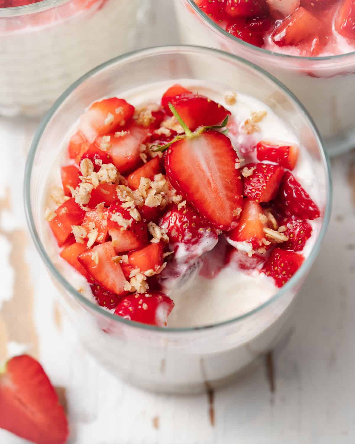 a bite taken off no bake cheesecake in a cup that is topped with fresh chopped strawberries.