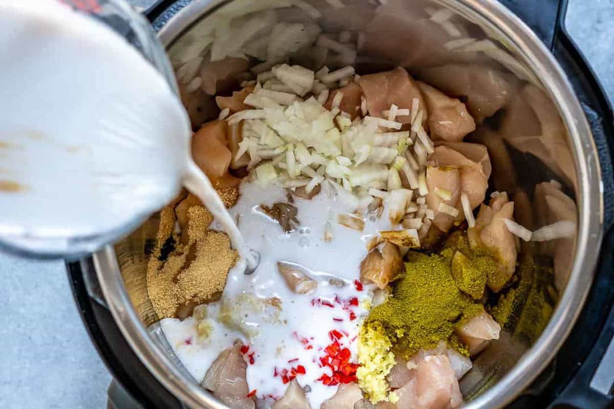 milk being poured in the Instant Pot with chicken curry ingredients/