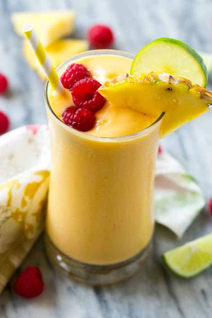 a cup filled with tropical smoothie topped with raspberry and slice of pineapple with a straw in the cup.