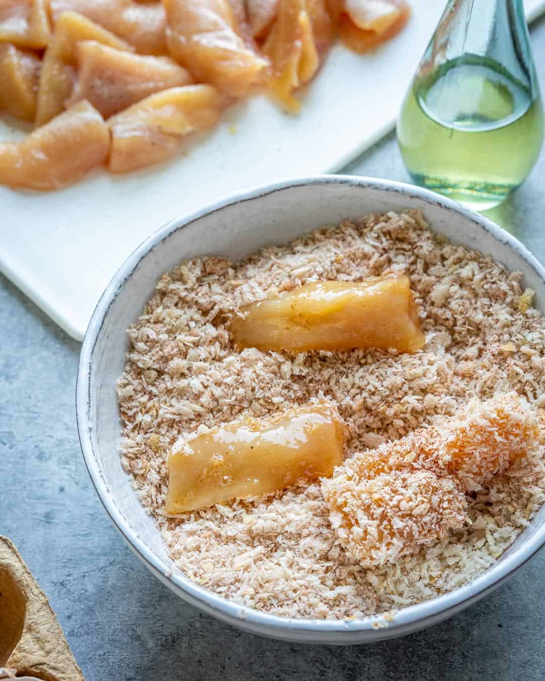 Close view of chicken being coated in breadcrumbs. 