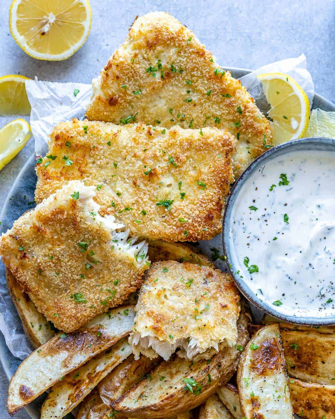 Top view of fish and chips on plate with lemon wedges. 