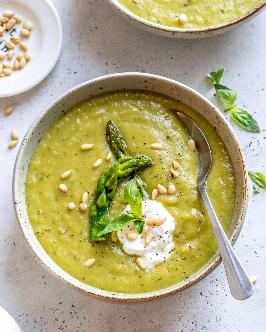 Bowl of asparagus soup garnished with yogurt, basil, and pine leaves