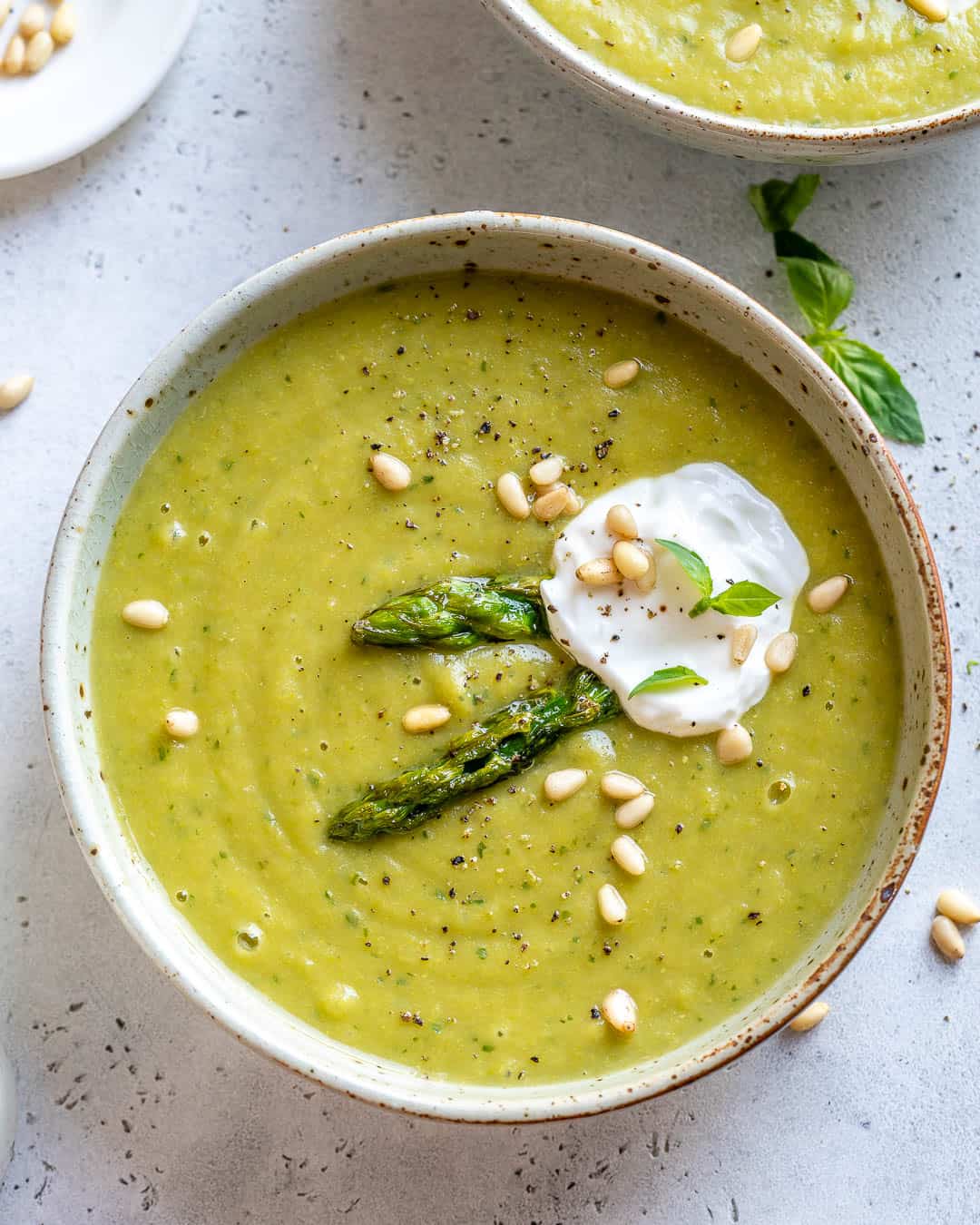 Bowl of Health Asparagus Soup garnished with yogurt, pine nuts, and basil.