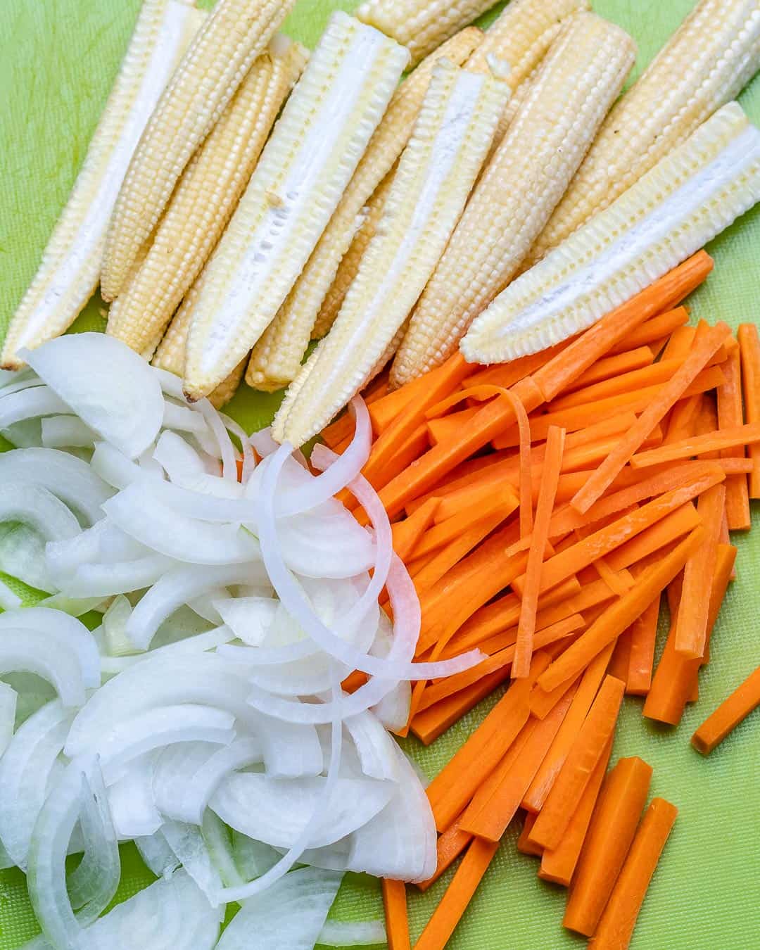 Carrots, onions, and baby corn on cutting board