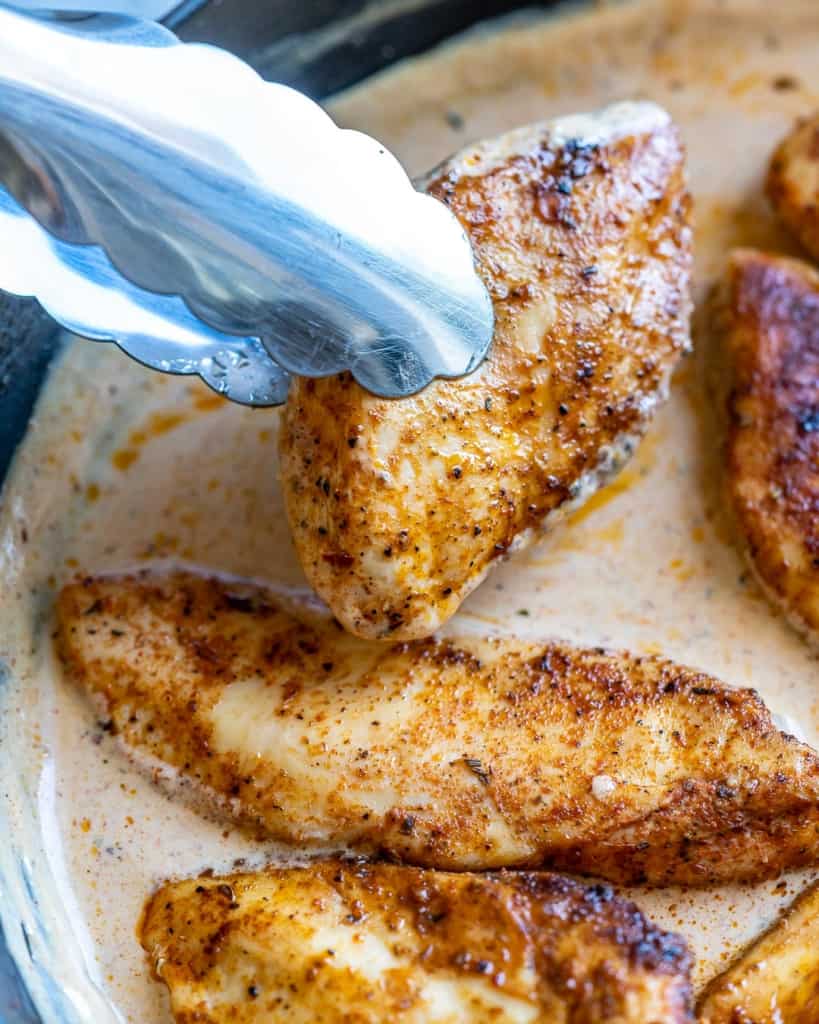 sauteed seasoning chicken breast being added into the cajun creamy sauce in pan
