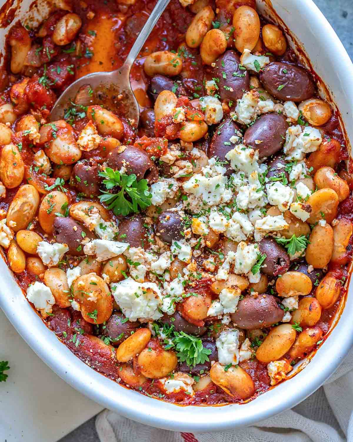 oval dish with baked beans greek style, topped with crumbled feta cheese and chopped parsley.