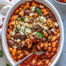 oval dish with Greek baked beans topped with crumbled feta and chopped parsley.