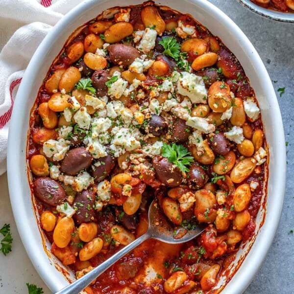 oval dish with Greek baked beans topped with crumbled feta and chopped parsley.