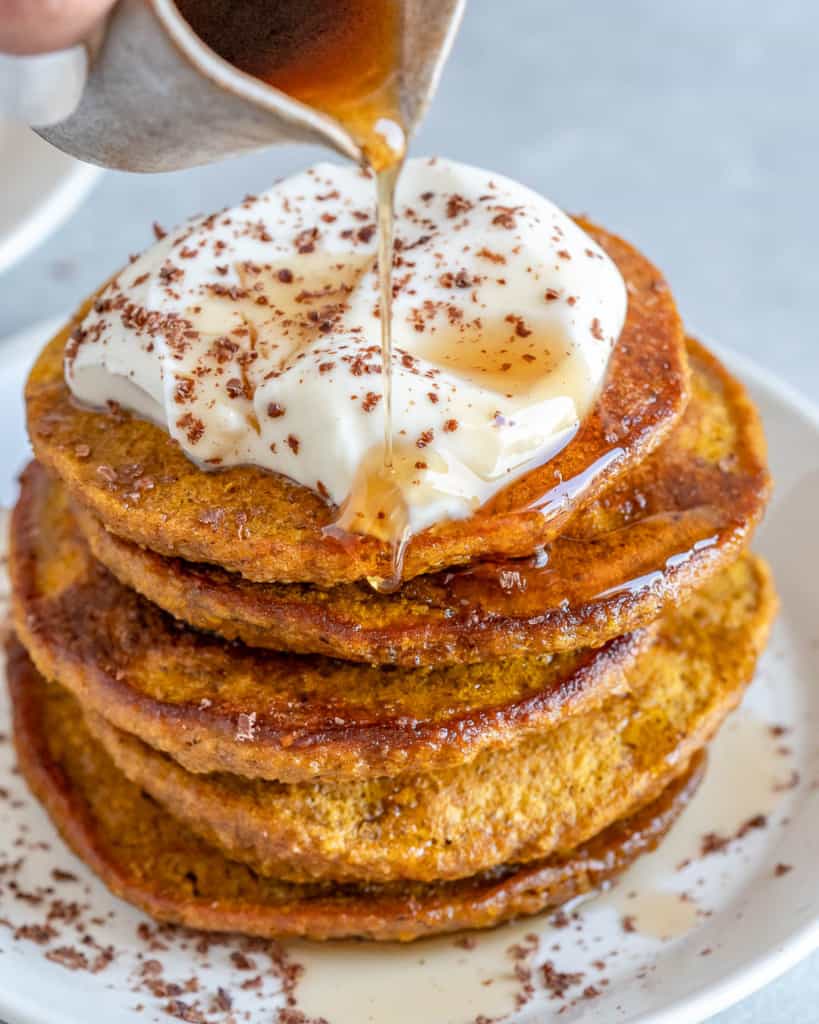 easy pumpkin pancakes with yogurt topping and maple being drizzled over the pancakes 