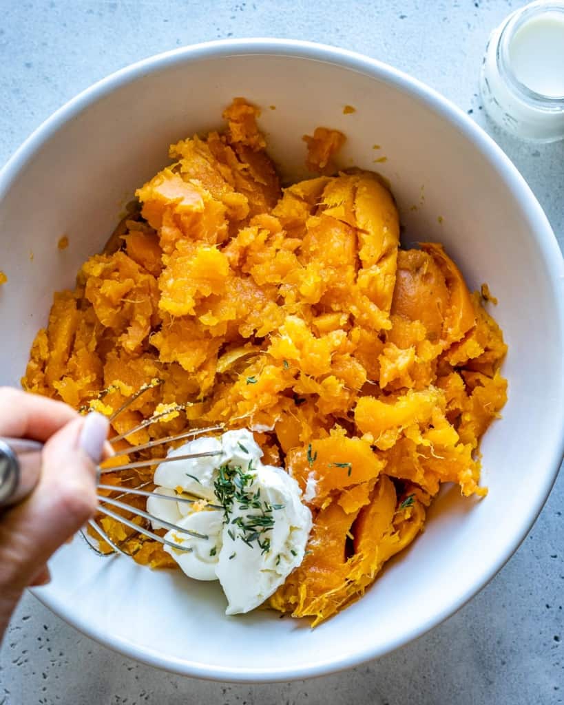 mashed sweet potato in white bowl with cream cheese being whisked in