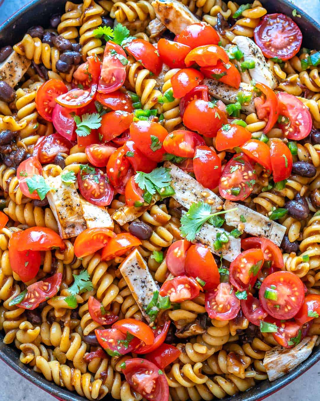 Close up of tomatoes and cilantro toppings on pasta in pot. 