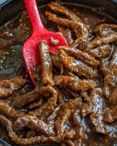 sauteed beef with Mongolian sauce on a pan with a red spoon in skillet