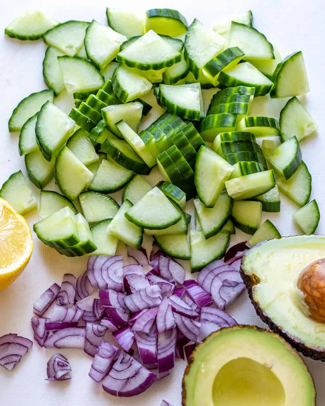 Chopped cucumbers, onions, and avocado on cutting board