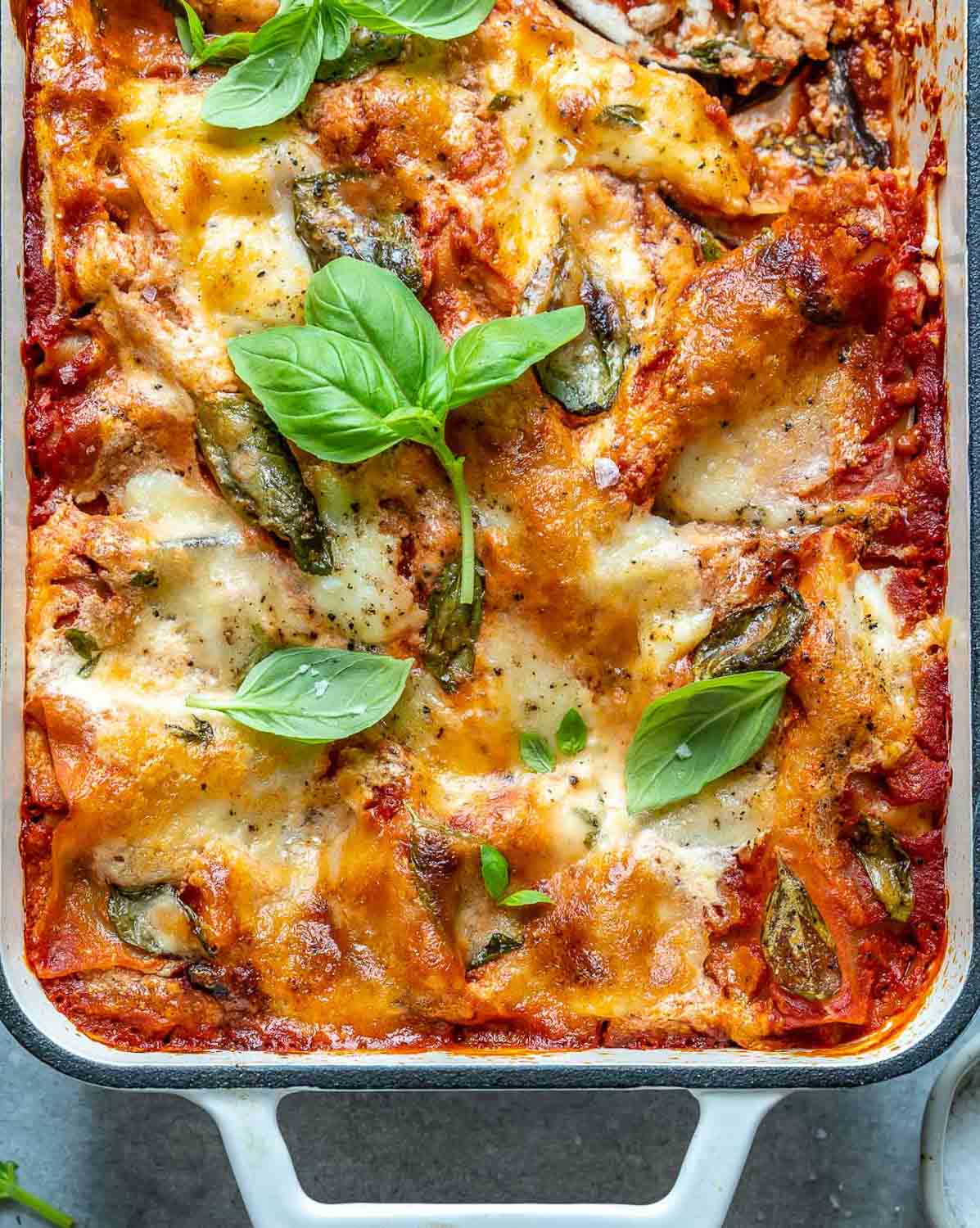 eggplant lasagna baked in a white dish topped with fresh basil.