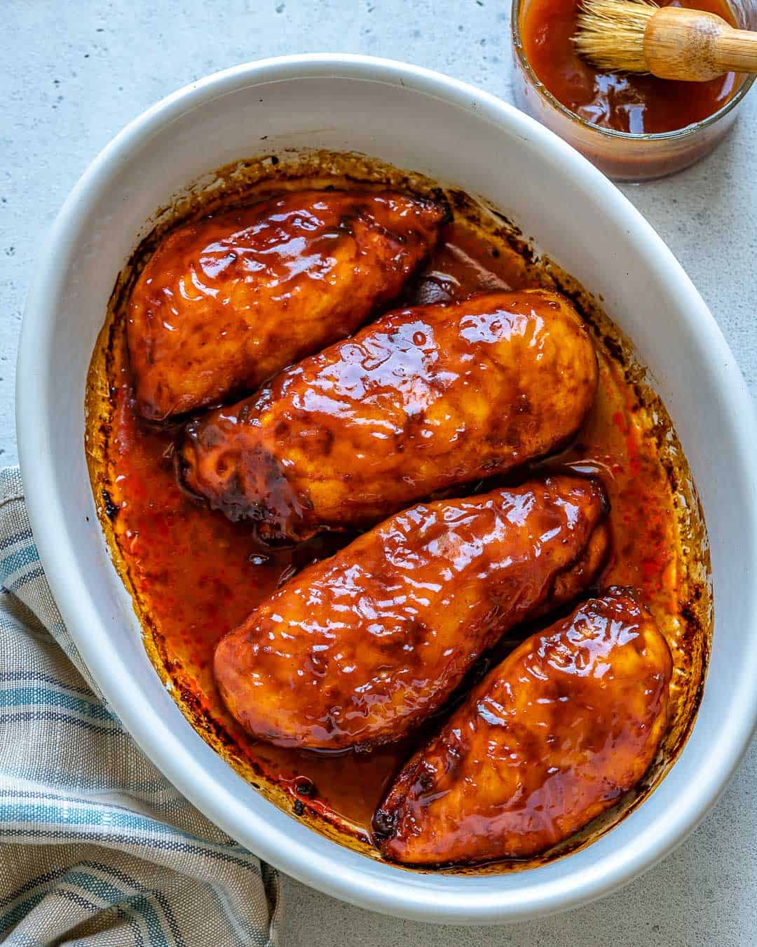 Top view of white baking dish with 4 Baked BBQ Chicken Breasts and bowl of BBQ sauce on side