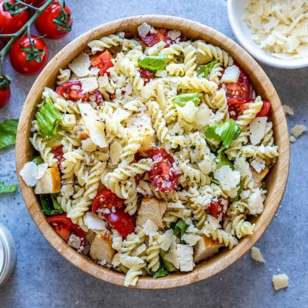 chicken pasta salad in a round brown bowl with lettuce, pasta, chicken, and tomatoes.