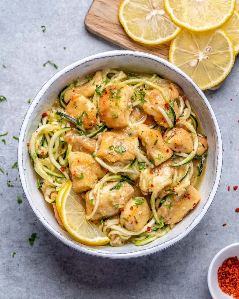 chicken scampi and zoodles in a white bowl with lemon slices on the side 