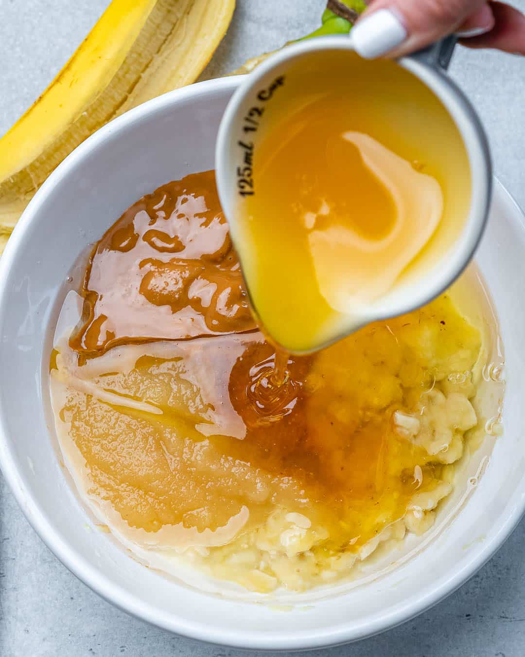 Hand pouring honey into bowl of wet ingredients for muffins.
