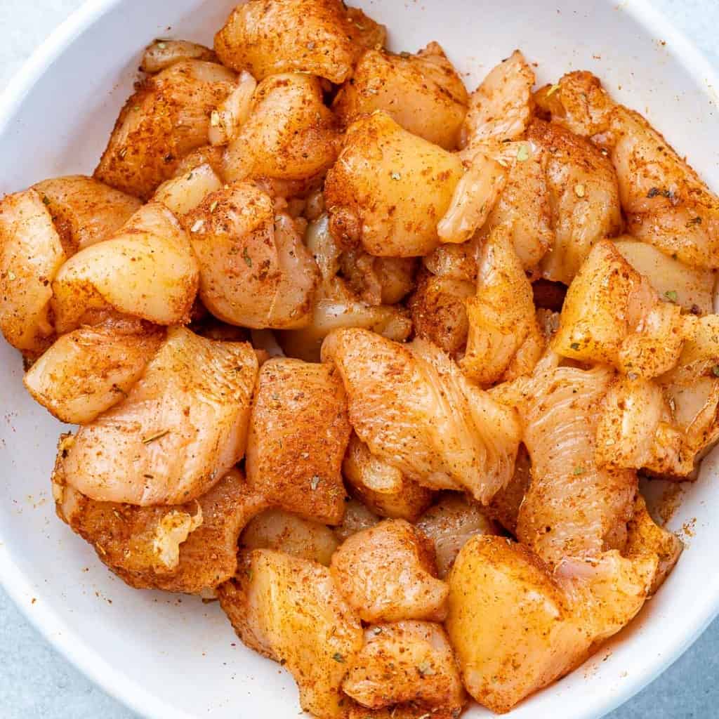seasoned chicken bites in a white bowl before cooking 