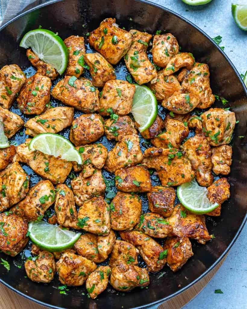 top view of chicken bites with lime wedges in a skillet