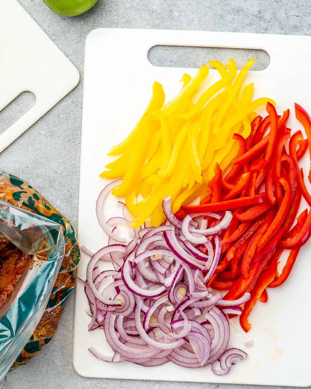 Sliced bell pepper and onion on cutting board for chicken fajitas. 