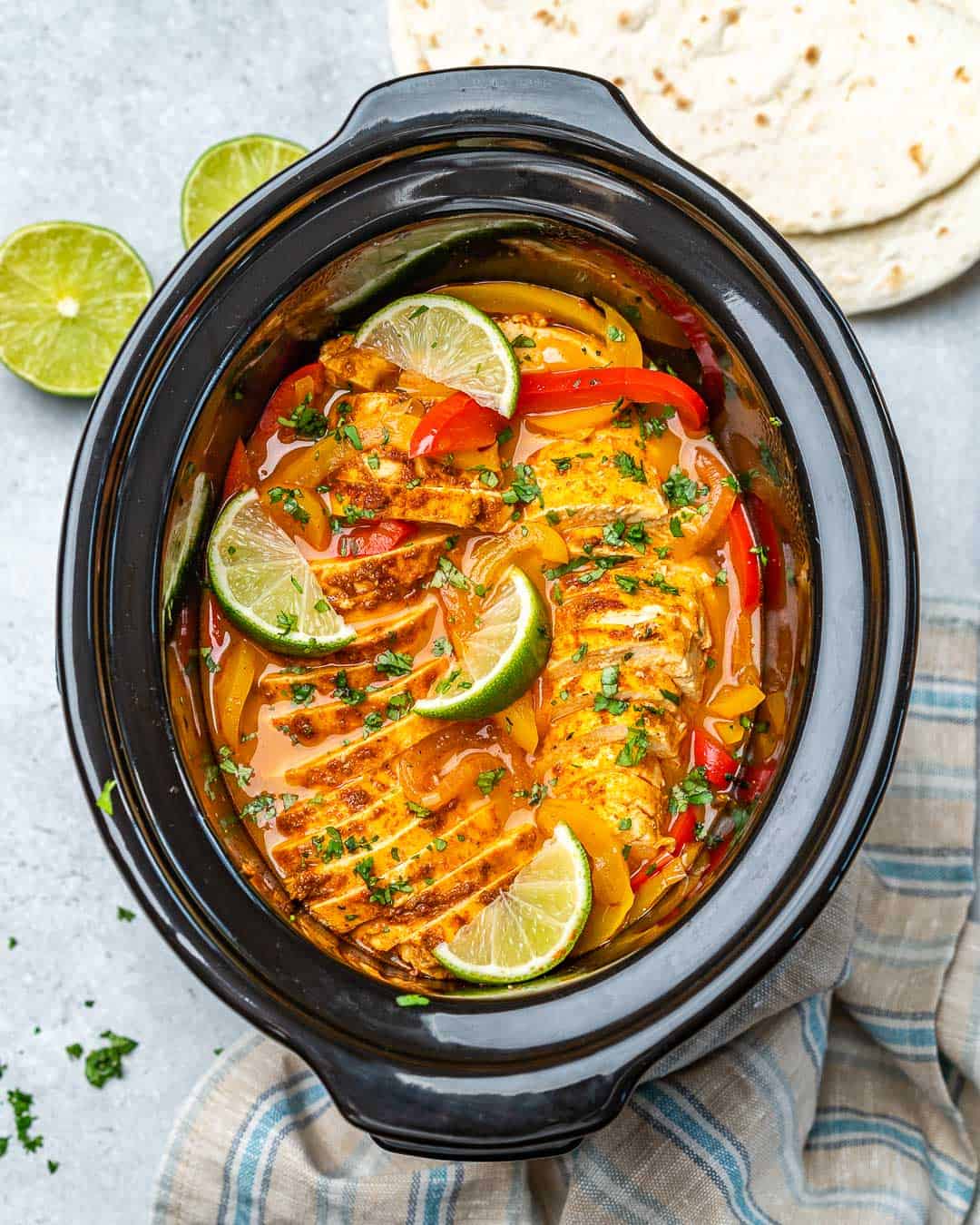 Crockpot chicken fajitas with tortillas and limes on counter.